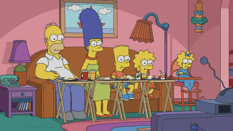 Homer, Marge, Bart, Lisa, and Maggie eating dinner on their couch in front of the TV in The Simpsons