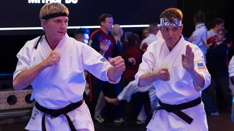 Johnny Lawrence (William Zabka) and Daniel LaRusso (Ralph Macchio) take fighting poses while wearing karate gis in Cobra Kai