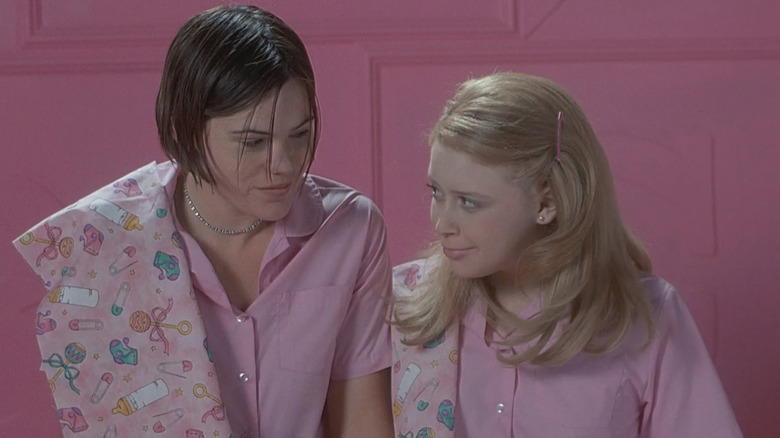 Clea DuVall as Graham Eaton and Natasha Lyonne as Megan Bloomfield looking at each other and smiling while practicing with baby dolls in a pink room in But I'm a Cheerleader