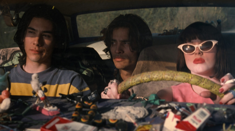 James Duval as Jordan White in the front passenger seat, James Duval as Jordan White in the back seat, and Rose McGowan as Amy Blue driving and smoking in The Doom Generation