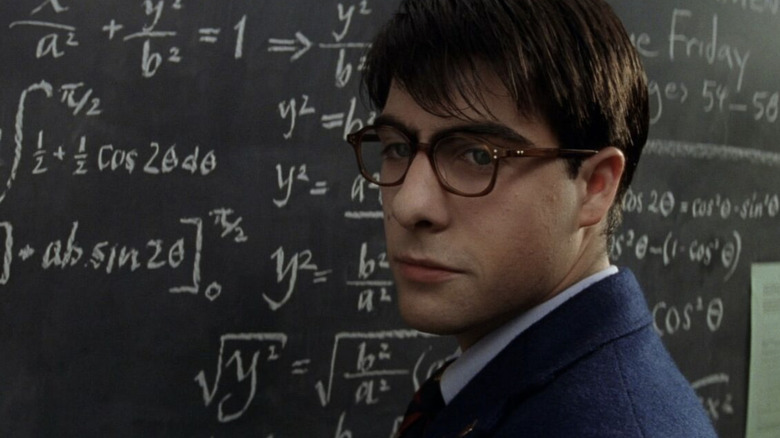 Jason Schwartzman as Max Fischer wearing glasses and standing in front of a math chalkboard in Rushmore