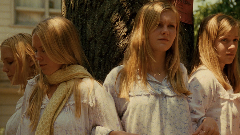 A.J. Cook as Mary Lisbon, Hanna R. Hall as Cecilia Lisbon, Kirsten Dunst as Lux Lisbon, and Leslie Hayman as Therese Lisbon linking arms in front of a tree in The Virgin Suicides