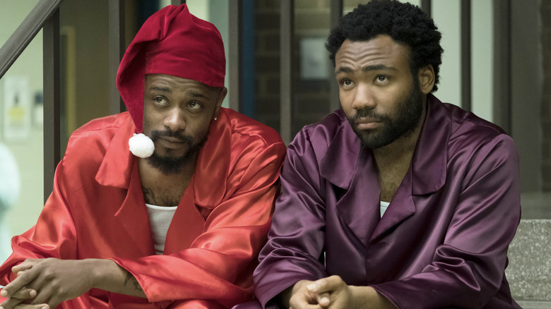LaKeith Stanfield as Darius wearing red silk pajams and a night cap sitting next to Donald Glover as Earnest "Earn" Marks wearing pruple silk pajamas in Atlanta