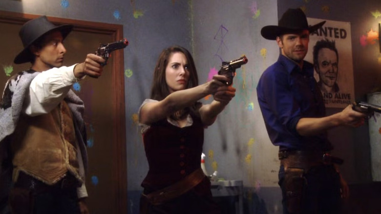 Danny Pudi as Abed Nadir, Alison Brie as Annie Edison, and Joel McHale as Jeff Winger dressed in western clothes while holding paintball guns in Community