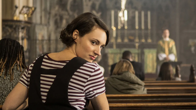 Phoebe Waller-Bridge as "Fleabag" wearing black and white stripes while sitting in a pew at church during a sermon by Andrew Scott as The Hot Priest Fleabag