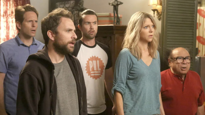 Glenn Howerton as Dennis Reynolds wearing a blue shirt, Charlie Day as Charlie Kelly wearing a hoodie, Rob McElhenney as Ronald "Mac" McDonald wearing a PHL shirt, Kaitlin Olson as Deandra "Sweet Dee" Reynolds, wearing a teal shirt, and Danny DeVito as Frank Reynolds wearing a red shirt all looking confused in  It's Always Sunny in Philadelphia
