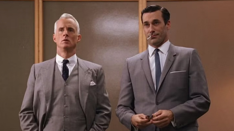 John Slattery as Roger Sterling and Jon Hamm as Don Draper wearing suits and smoking while standing up in Mad Men