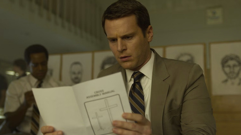 Jonathan Groff as Holden Ford wearing a suit and tie while reading a religious pamphlet with a cross on the front in Mindhunter