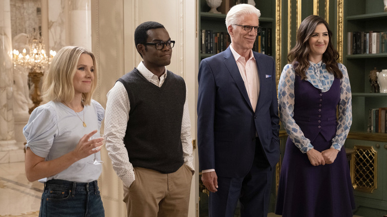 Kristen Bell as Eleanor Shellstrop wearing a blue shirt, William Jackson Harper as Chidi Anagonye weairing a black vest, Ted Danson as Michael wearing a blue suit, and  D'Arcy Carden as Janet wearing a purple dress in The Good Place