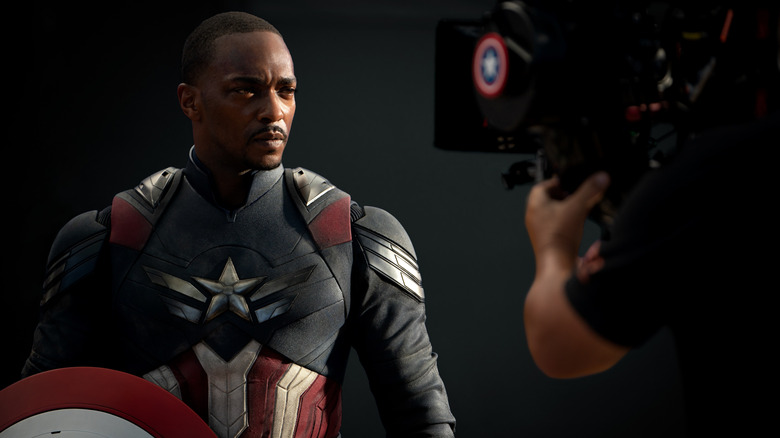Anthony Mackie as Sam Wilson suited up and standing with his shield in front of a camera in a behind-the-scenes still from the set of Captain America: Brave New World
