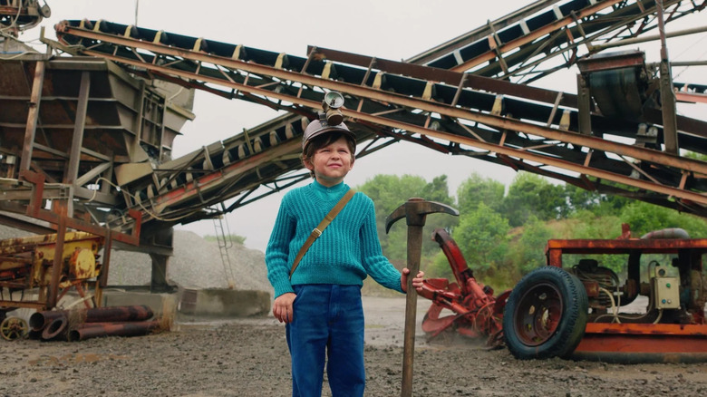 A young Steve holding a pickaxe next to some mining equipment in A Minecraft Movie
