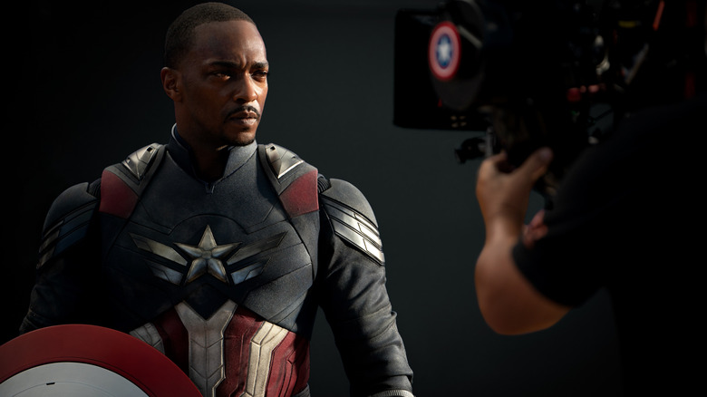 Anthony Mackie as Sam Wilson suited up and standing with his shield in front of a camera in a behind-the-scenes still from the set of Captain America: Brave New World