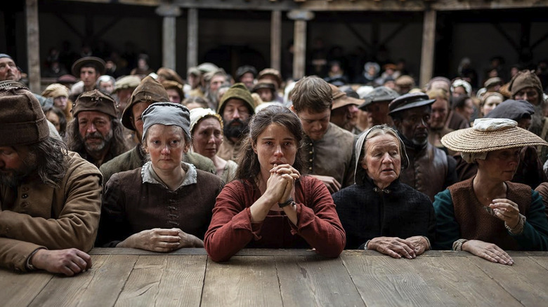 Agnes in the front row at the Globe theater with her hands clasped in front of her in Hamnet