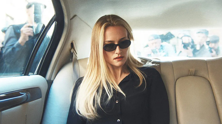 Carolyn sitting in the back of a car wearing sunglasses in Love Story: John F. Kennedy Jr. & Carolyn Bessette