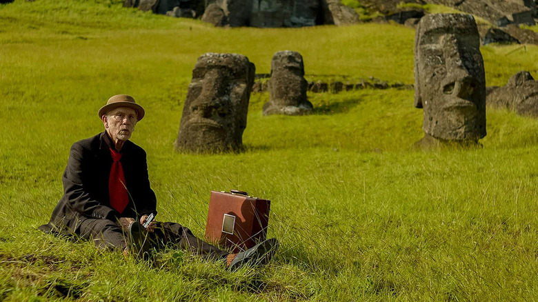 Chris sitting next to a suitcase in front of Easter Island heads in Wild Horse Nine