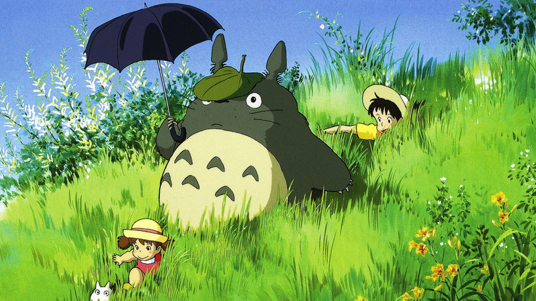 Satsuki (Noriko Hidaka) and Mei (Chika Sakamoto) walk with Totoro (Hitoshi Takagi) on a grassy hill in My Neighbor Totoro