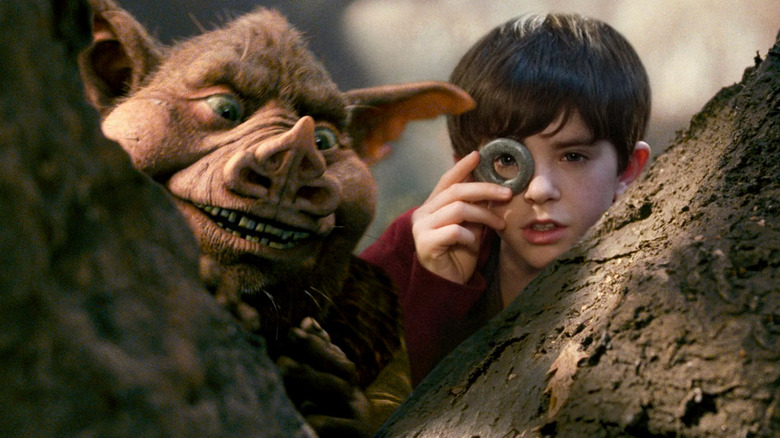 Jared Grace (Freddie Highmore) looks through a seeing stone with Hogsqueal next to him in a forest in The Spiderwick Chronicles