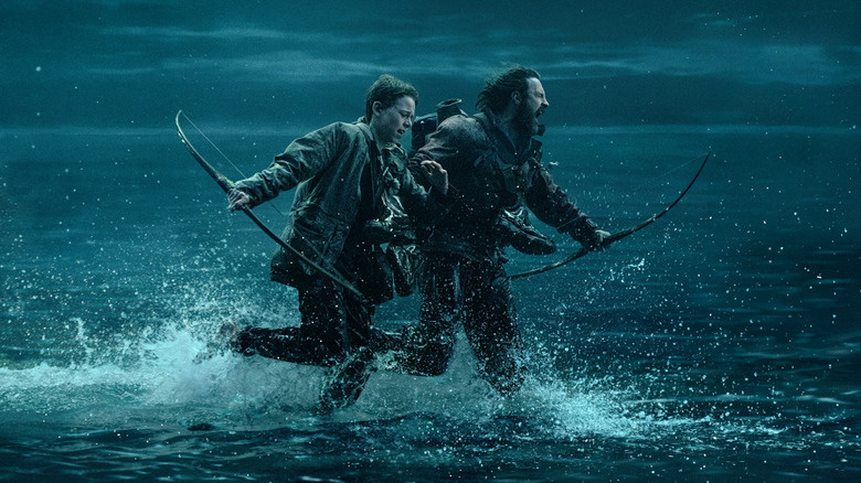 Aaron Taylor-Johnson as Jamie and Alfie Williams as his son Spike running across shallow waters away from danger in 28 Years Later