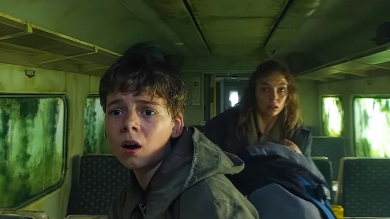 28 Years Later, Isla holding baby Isla in the train, standing behind Spike