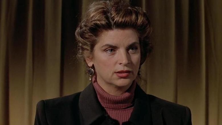 Kirstie Alley as Dr. Susan Verners standing in front of a cutain in a red sweater in Village of the Damned (1995)