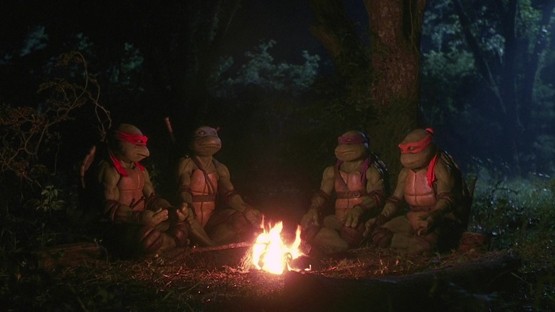 Raphael, Leonardo, Donatello, and Michaelangelo sitting by a fire in Teenage Mutant Ninja Turtles (1990)