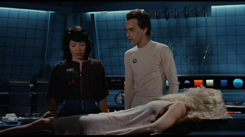 Don Opper as Max 404 shows off Kendra Kirchner as Cassandra to Maggie as Brie Howard in Android