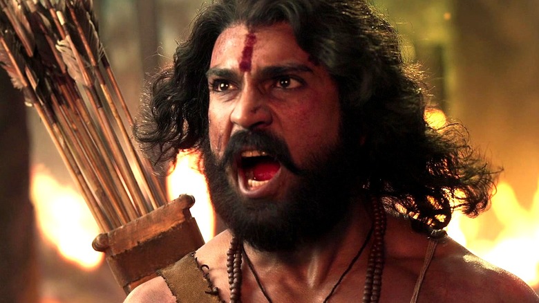 Ram Charan as Alluri Sitarama Raju with his quill on his back in front of flames in RRR