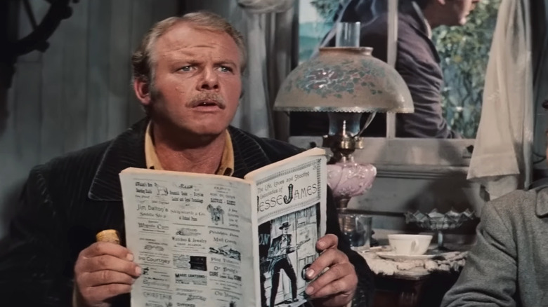 Alan Hale Jr.'s Cole Younger looks up while holding a newspaper in The True Story of Jesse James
