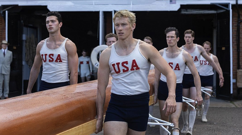 Joe Rantz and his team carry a boat together while wearing USA shirts in The Boys in the Boat