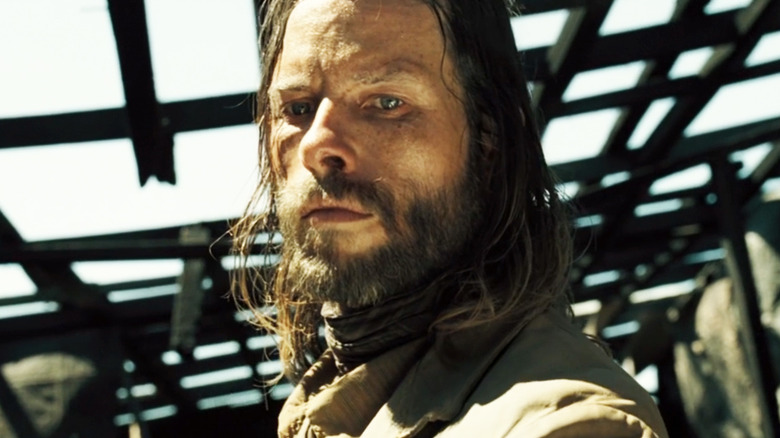 Guy Pearce's Charlie Burns is seen from a low angle ashe stands beneath wooden beams in The Proposition