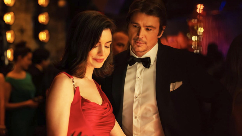 Verity wears a red dress and stands next to a tuxedo-wearing Jeremy in Verity