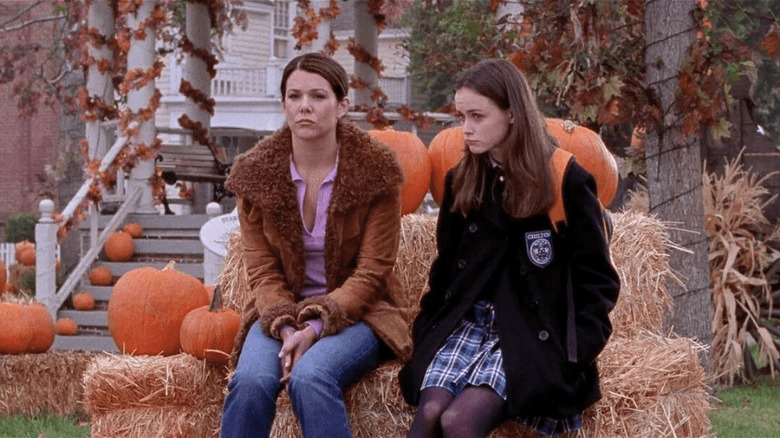 Lorelai and Rory sitting on a bale of hay in front of pumpkins on Gilmore Girls