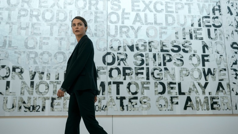 Kate walking past a wall with political words all over it in The Diplomat