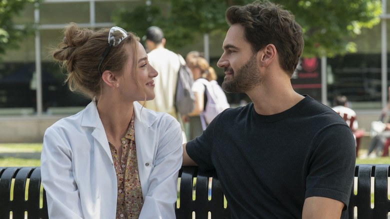 Olive and Adam on a bench smiling at each other in The Love Hypothesis