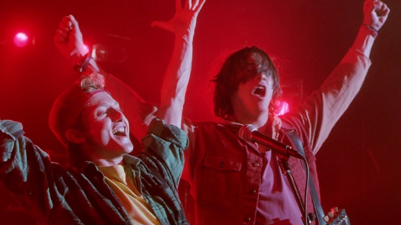 Alex Winter as Bill and Keanu Reeves as Ted cheering on a stage bathed in red light in Bill & Ted's Bogus Journey