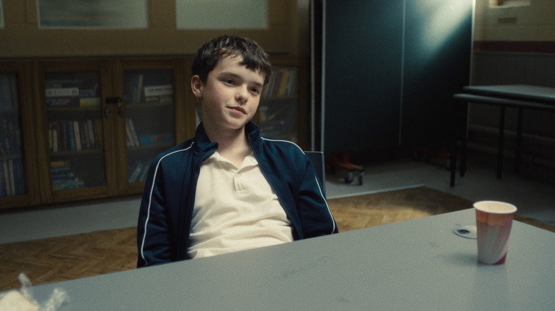 Owen Cooper as Jamie Miller smirking at a table in Adolescence