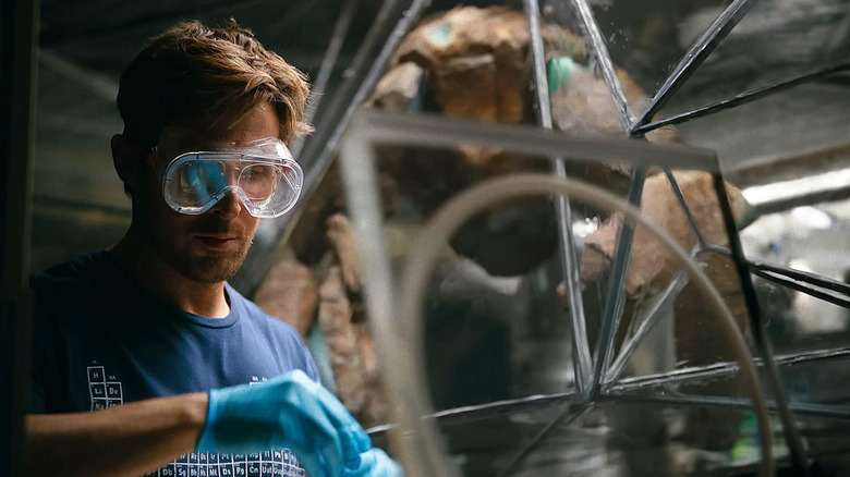 Ryan Gosling as Ryland Grace wearing protective goggles and conducting an experiment as James Ortiz as the voice of Rocky observes behind him in Project Hail Mary