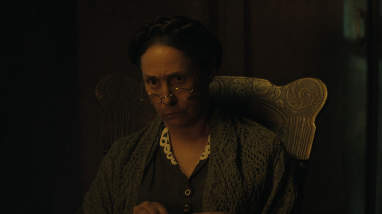 Augusta wearing glasses sitting in a rocking chair on Monster: The Ed Gein Story