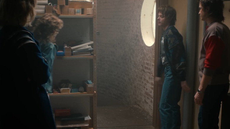 Robin Buckley (Maya Hawke), Nancy Wheeler (Natalia Dyer), Jonathan (Charlie Heaton), and Steve (Joe Keery) stood in front of a secret door in Stranger Things