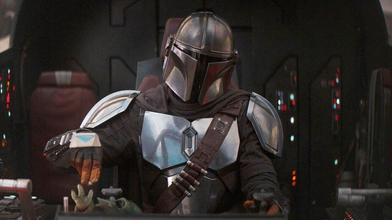 Pedro Pascal as Din Djarin in the cockpit of his ship while Grogu plays with his hand in The Mandalorian