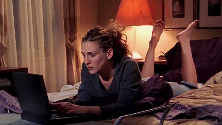 Carrie writing on her laptop on her bed in Sex and the City