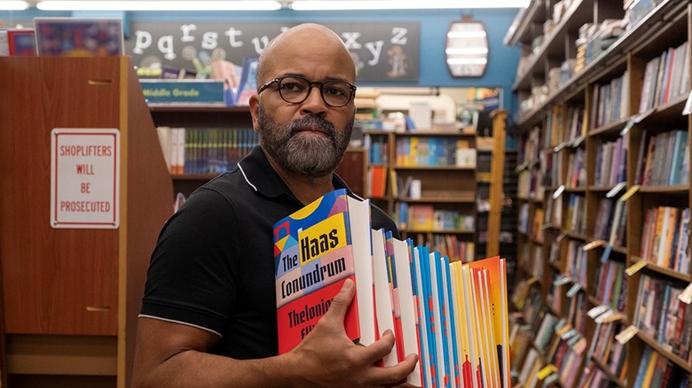 Monk Ellison holding a stack of his books in a bookstore in American Fiction