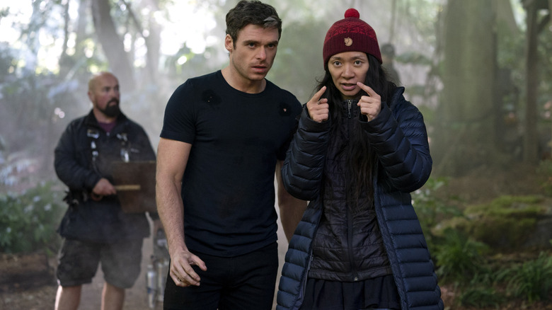 Director Chloé Zhao standing next to Richard Madden as Ikaris in a forest on the set of Eternals