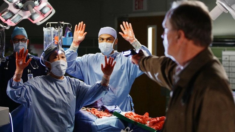 Cristina and Jackson holding up their hands in surrender while Gary Clark points a gun on Grey's Anatomy