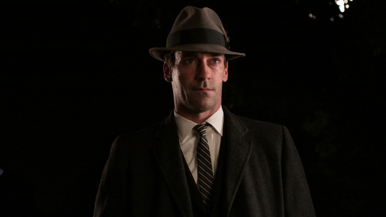 Don wearing a hat and looking serious in near darkness on Mad Men