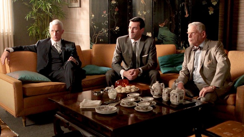 Roger Don and Bert on a couch at a hotel listening to someone on Mad Men