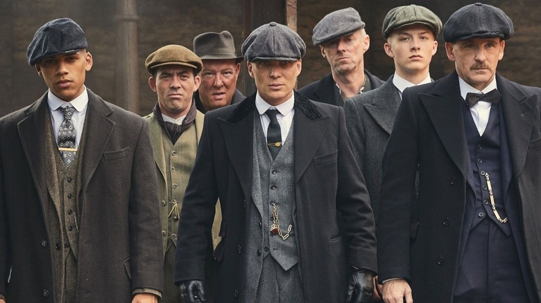 Jordan Bolger as Isiah, Packy Lee as Johnny Dogs, Ian Peck as Curly, Cillian Murphy as Tommy Shelby, Ned Dennehy as Charlie Strong, Harry Kirton as Finn Shelby, and Paul Anderson as Arthur Shelby wearing suits and walking down a road in Peaky Blinders