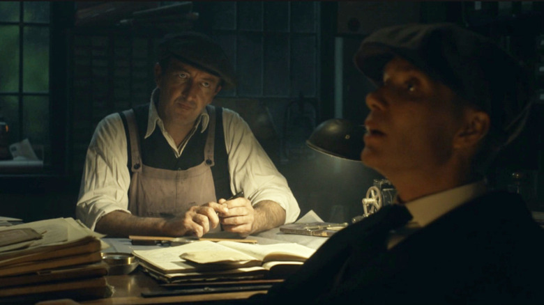 Ralph Ineson as Connor Nutley seated behind a desk and staring at Cillian Murphy as Tommy Shelby in Peaky Blinders