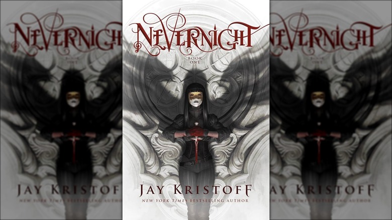 Mia Corvere standing in a mask holding a knife with shadow wings on the wall behind her on the cover of Nevernight