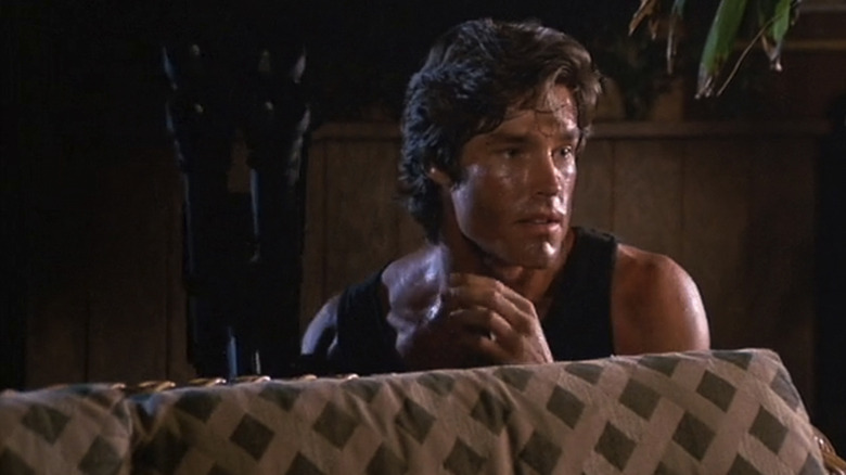 Ronn Moss as Roddy Abilene crouched behind a couch in Hard Ticket to Hawaii